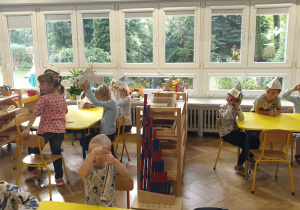 Na zdjęciu widzimy grupkę dzieci, która na siedzi przy stolikach i ma na głowach własnoręcznie wykonane czapki z gazety.