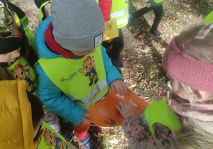 Zdjęcie przedstawia dzieci przyklejające liście do pomarańczowej kartki.