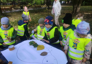 Zdjęcie przedstawia dzieci przyklejające zebrane liście na sylwetę jeża.