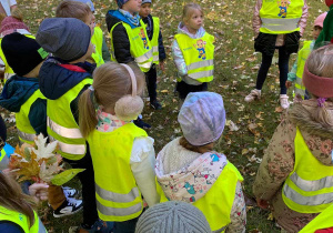 Zdjęcie przedstawia grupę dzieci w parku. Dzieci mają na sobie kamizelki odblaskowe.