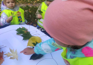 Zdjęcie przedstawia dziewczynkę przyklejającą liście na sylwecie jeża.