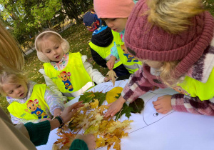 Zdjęcie przedstawia dzieci przyklejające liście na sylwecie jeża.