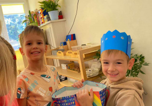 Zdjęcie przedstawia dwóch chłopców uśmiechających się do zdjęcia. Jeden z nich ma na głowie niebieską koronę.