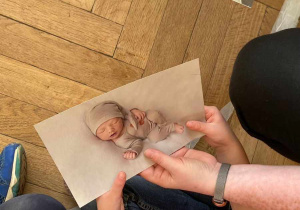 Zdjęcie przedstawia zdjęcie noworodka trzymane w dłoni.
