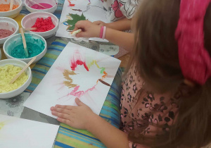 Zdjęcie przedstawia dziewczynkę, która odrysowała liścia z wykorzystaniem kredek pastelowych