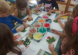 Na zdjęciu widać dzieci przy stoliku wykonujące prace plastyczną, bawiąc się kolorami