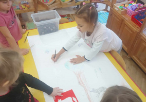 Zdjecie przedstawia współpracujące dzieci, które podzieliły się zadaniami do wykonania przy obrazie