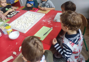 Dzieci kroją kluseczki leniwe z przygotowanego wałka ciasta