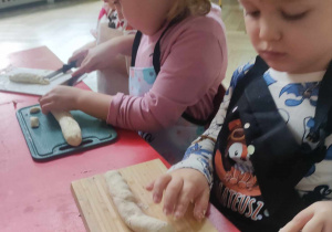 Dzieci kroją kluseczki leniwe z przygotowanego wałka ciasta