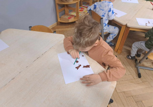 Zdjęcie przedstawia chłopca rozduchującego farbę przy pomocy rurki.