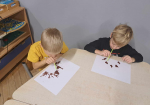 Zdjęcie przedstawia chłopców rozduchujących farbę przy pomocy rurek.