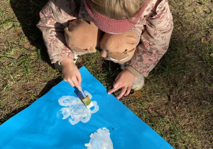 Dziecko maluje swoją chmurę na niebieskim tle.