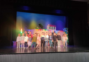 Zdjęcie przedstawia grupę dzieci stojących na scenie teatralnej.