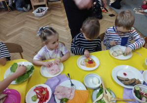 Na zdjęciu widzimy trójkę dzieci, która tworzy kolorowe kanapki.