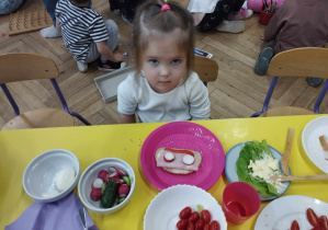 Na zdjęciu widzimy dziewczynkę, która na talerzyku przed sobą ma wykonaną kolorową kanapkę, z lubianych produktów.