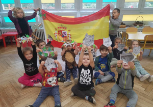Dzieci prezentujące swoje prace plastyczne zwierząt objętych ochroną na tle flagi Hiszpani.