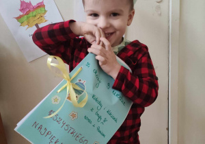 Zdjęcie przedstawia chłopca w koronie, który uśmiecha się do zdjęcia a w rękach trzyma urodzinową książeczkę.