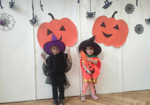 Zdjęcie przedstawia dwie dziewczynki w strojach na tle halloweenowej dekoracji.