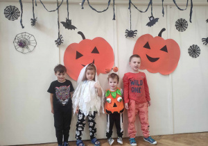 Zdjęcie przedstawia czworo dzieci w strojach na tle halloweenowej dekoracji.