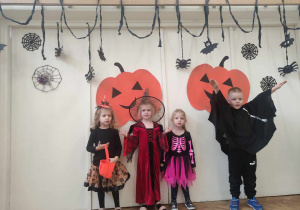 Zdjęcie przedstawia czworo dzieci w strojach na tle halloweenowej dekoracji.