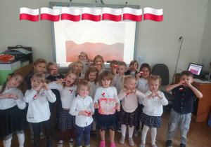 Zdjęcie przedstawia grupę dzieci ubranych na galowo z flagami Polski na bluzkach gotowych do wzięcia udziału w uroczystości