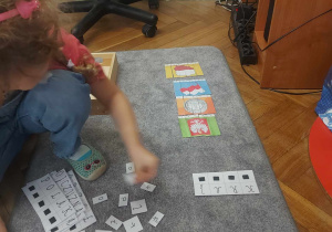 Na zdjęciu widac dziewczynkę, która na dywaniku układa wyrazy z rozsypanki literowej i ułożyła puzzle