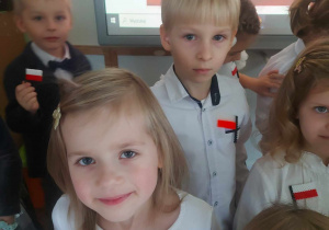 Zdjęcie przedstawia grupę dzieci ubranych a galowo, a na bluzkach mają biało czerwone flagi, które wykonały z koralików
