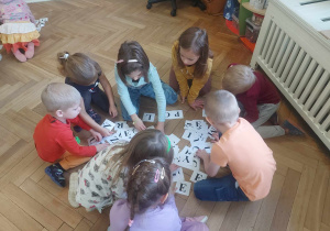 Na zdjęciu widać grupę dzieci, która z rozsypanki literowej mają za zadanie ułożyć wyrazy