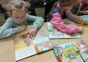 Na zdjęciu widzimy grupkę dziewczynek, które oglądają książki dla dzieci.