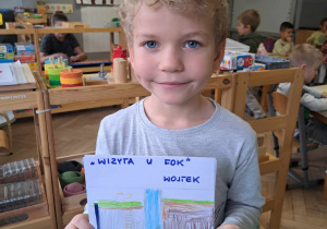 Zdjęcie przedstawia chłopca, trzymającego zrobioną przez siebie książkę.