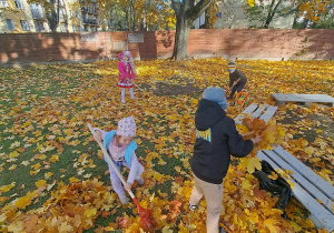 Zdjęcie przedstawia dzieci grabiące i zbierające liście.