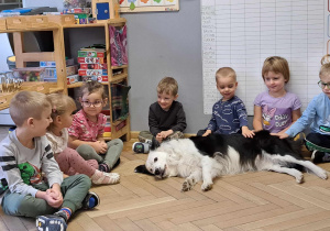 Zdjęcie przedstawia psa leżącego koło dzieci, które go głaszczą.
