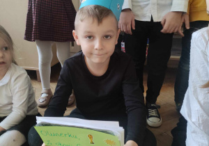 Zdjęcie przedstawia chłopca w niebieskiej koronie. Chłopiec trzyma w ręku urodzinową książeczkę.