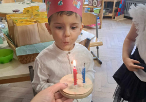 Zdjęcie przedstawia chłopca dmuchającego świeczkę.