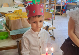 Zdjęcie przedstawia chłopca z tortem z zapalonymi świeczkami.