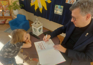 Zdjęcie przedstawia Pana marka, który pisze dedykację dla małego chłopca