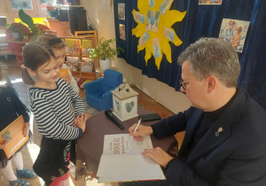 Zdjęcie przedstawia Pana Marka, który wpisuje dedykację dla dziewczynki