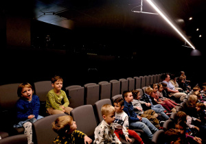 Zdjęcie przedstawia dzieci siedzące na fotelach w sali teatralnej.