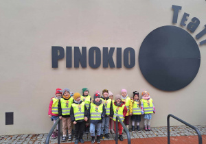 Zdjęcie przedstawia dzieci stojące przed teatrem, przy napisie "Teatr Pinokio"