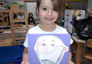 Zdjęcie przedstawia dziewczynkę trzymającą w ręku narysowany przez siebie portret Janusza Korczaka.
