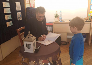 Zdjęcie przedstawia mężczyznę podpisującego książkę, dla chłopca stojącego obok.