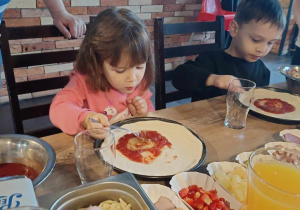 Dzieci polewają sosem pizzę.