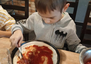 Chłopiec polewa sosem pizzę.