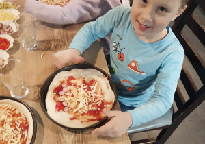 Chłopiec pokazuje zrobioną przez siebie pizzę.