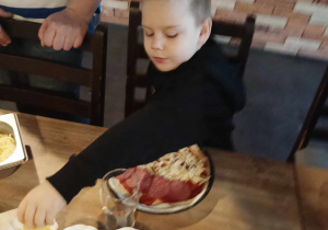 Chłopiec układa różne składniki na pizzę.