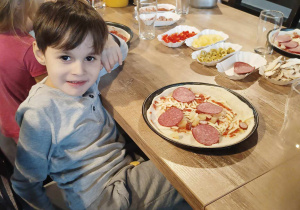 Chłopiec pokazuje zrobioną przez siebie pizzę.