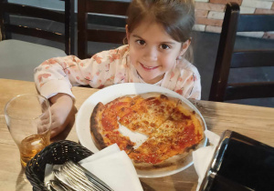 Dziewczynka pokazuje zrobioną przez sibie pizzę.