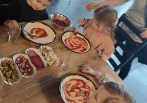Dzieci układają na pizzy ulubine składniki.