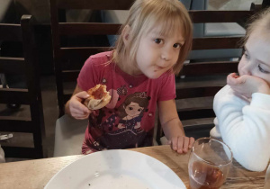Dziewczynka siedzi przy stole i je pizzę.