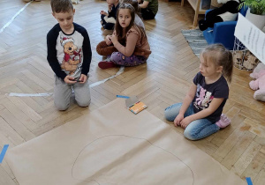 Dzieci rysują na dużym kartonie misia wg podanej instrukcji.